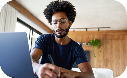 Rapaz com notebook e uma caneta na mão escrevendo algo