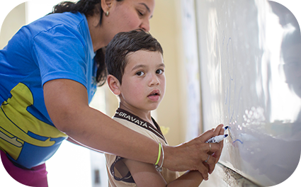 Moça ensinando criança em uma lousa.