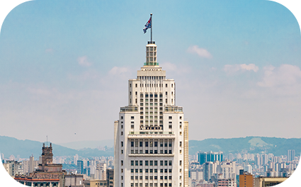 Um prédio grande ao centro em destaque com uma bandeira no topo e vários outros prédios menores ao redor