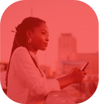 Mulher olhando a paisagem enquanto segura o celular em uma varanda, com alguns prédios desfocados ao fundo.