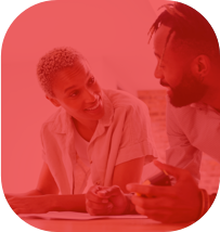 Casal conversando, olhando um para o outro e sorrindo enquanto estão apoiados em uma mesa.