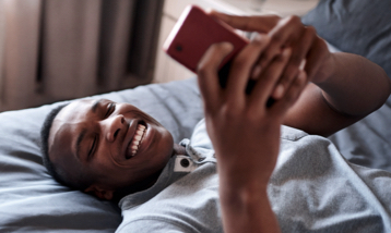 homem deitado na cama olhando seu celular